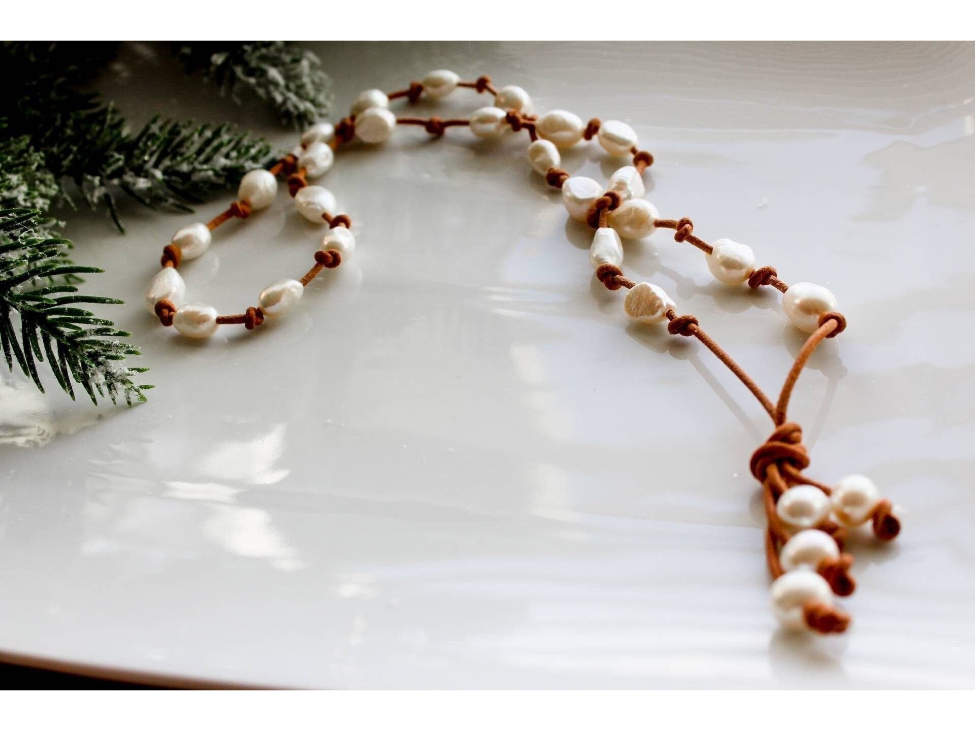 May include: A brown leather necklace with white pearl beads. The necklace has a tassel at the end.