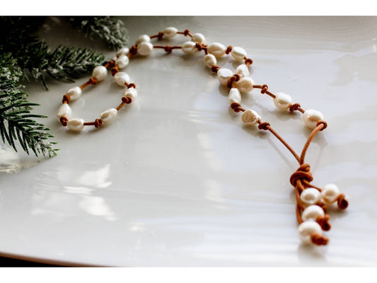 May include: A brown leather necklace with white pearl beads. The necklace has a tassel at the end.